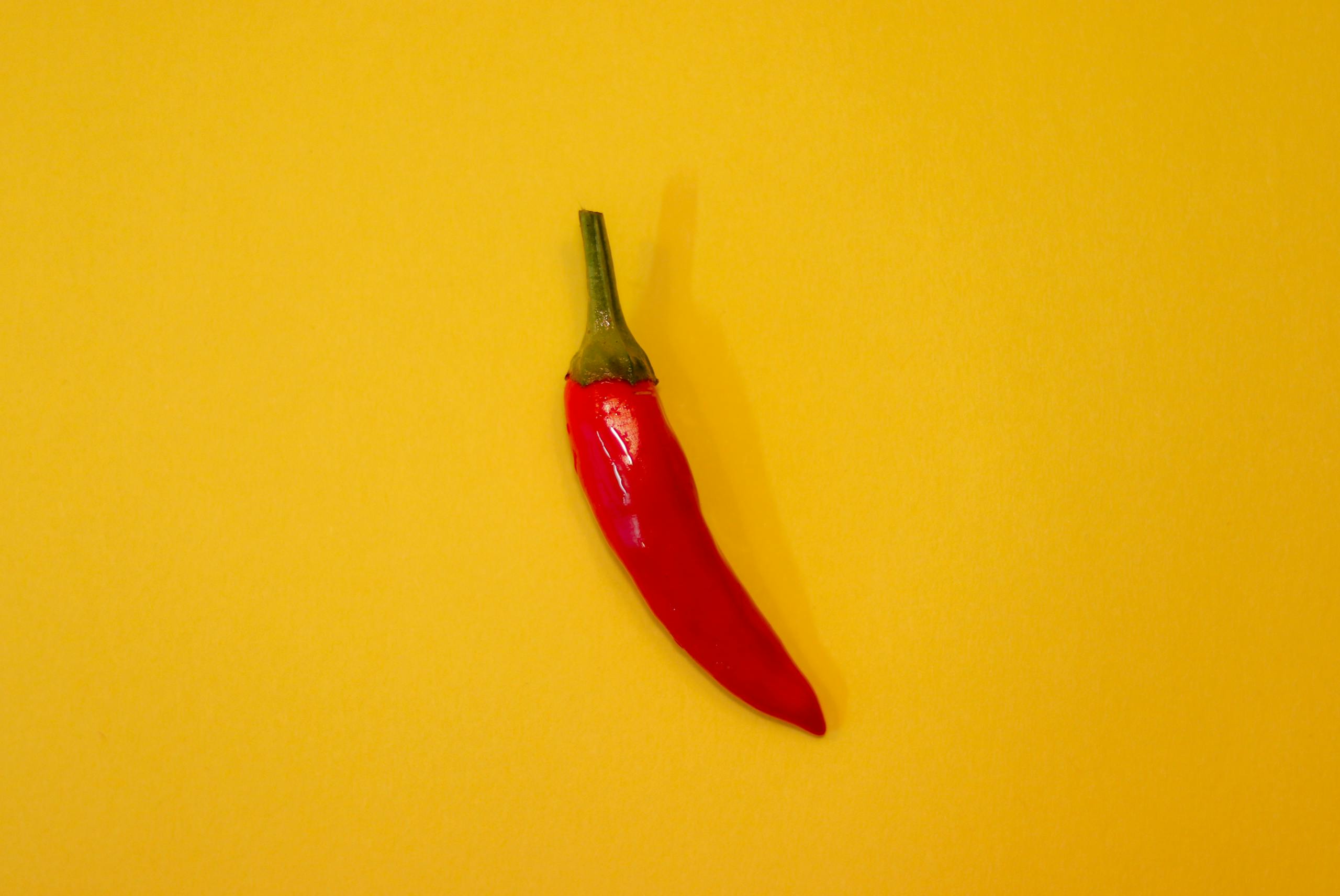 A single red chili pepper isolated on a vibrant yellow background, showcasing freshness and spice.